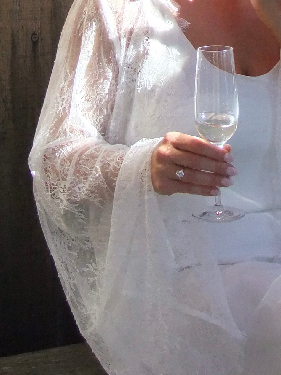 A bride's hand with an engagement ring, holding a glass of champagne