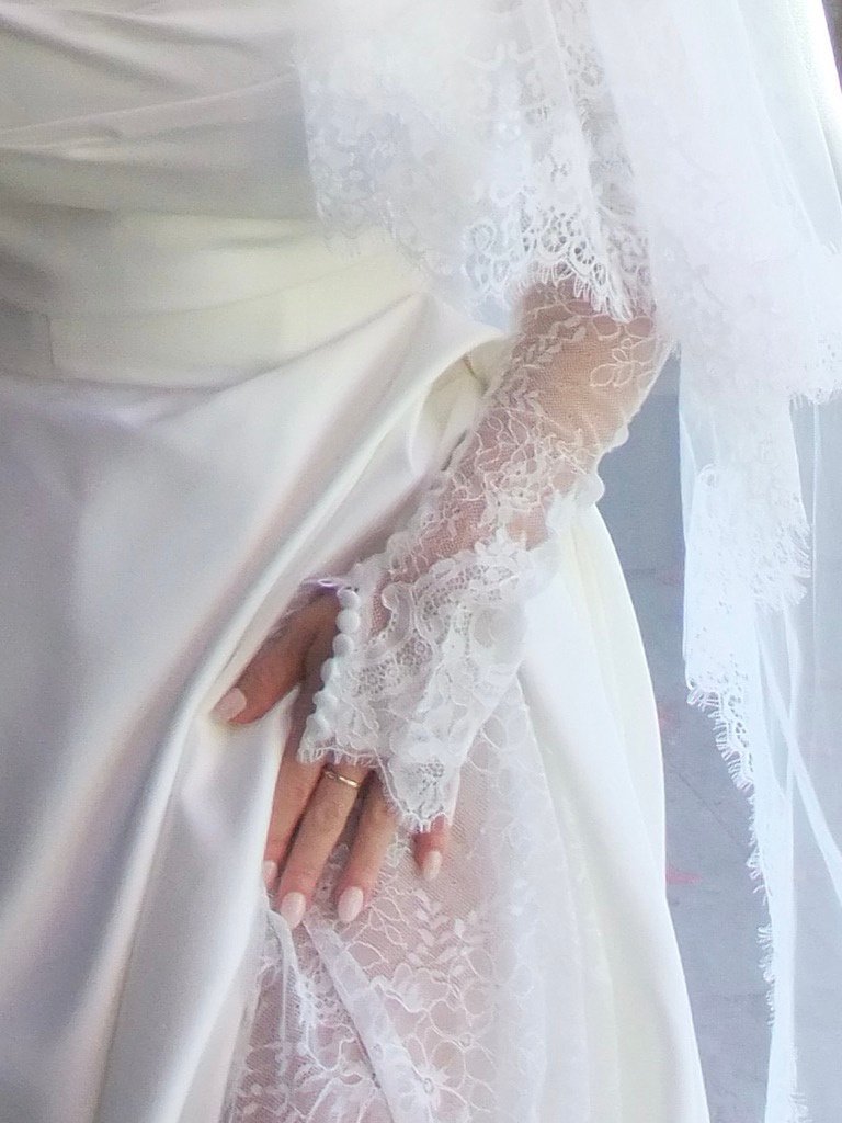 A bride's hand resting on a lace and satin wedding dress